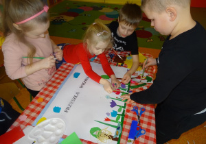 Dzieci dekorują plakat, naklejają kolorowe elementy z papieru.